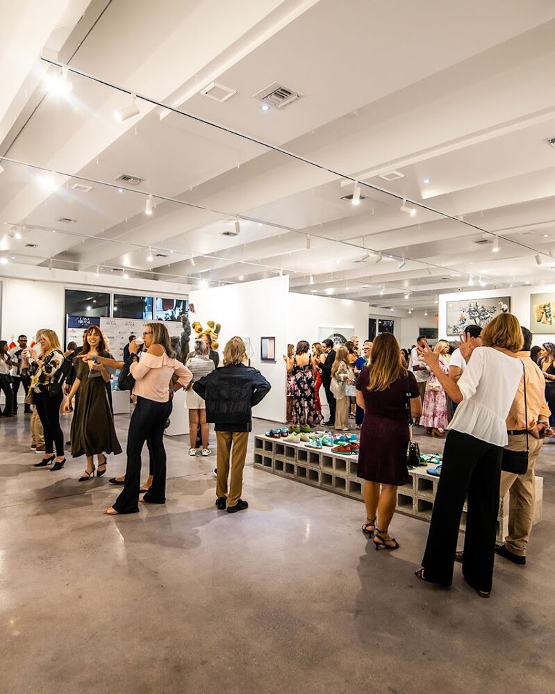A group of people are standing inside a gallery surrounded by artwork on display