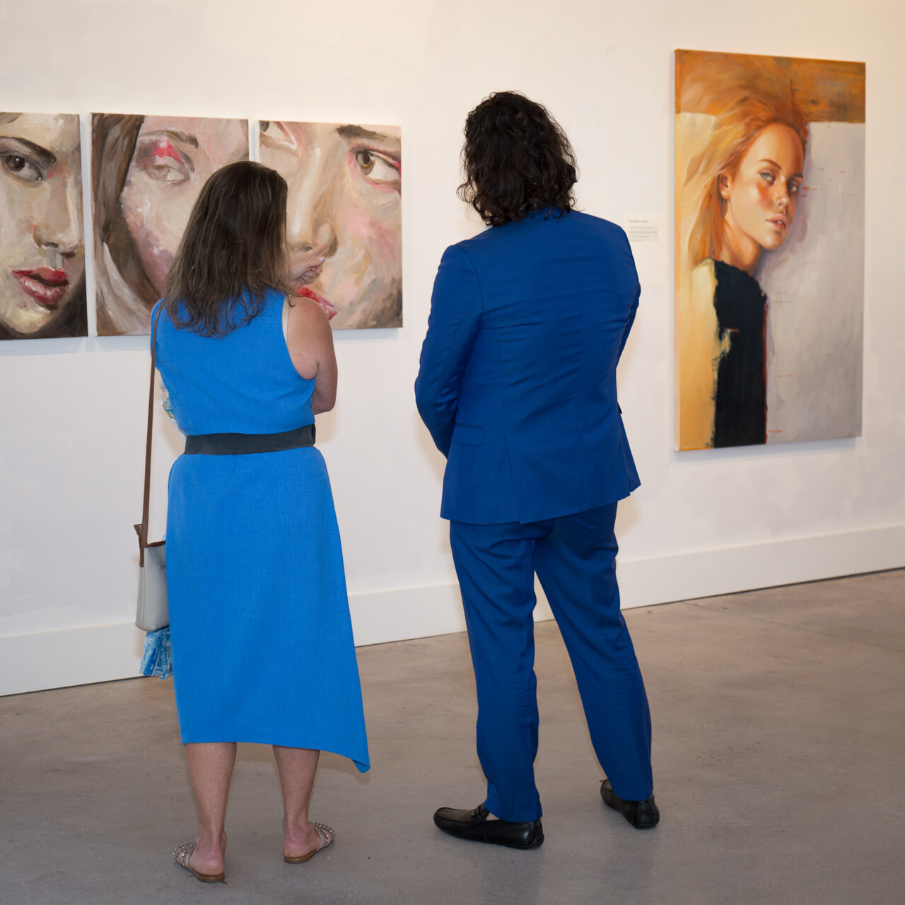 Artist Alex in a blue suit in conversation with art historian Luciane R. N. Garcez at an art exhibition