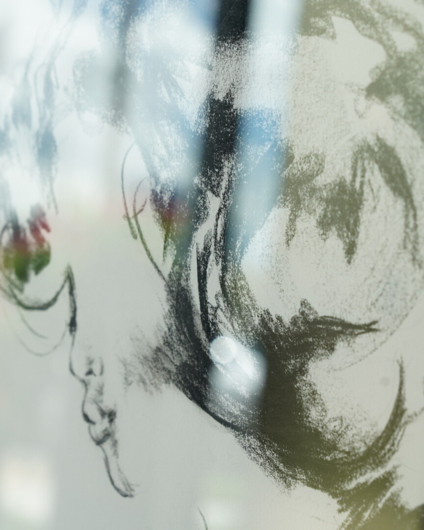 Un disegno a matita dell'artista Alex Righetto, che raffigura un volto astratto con una miscela di linee sfumate e un tocco di colore, esposto su una superficie riflettente.