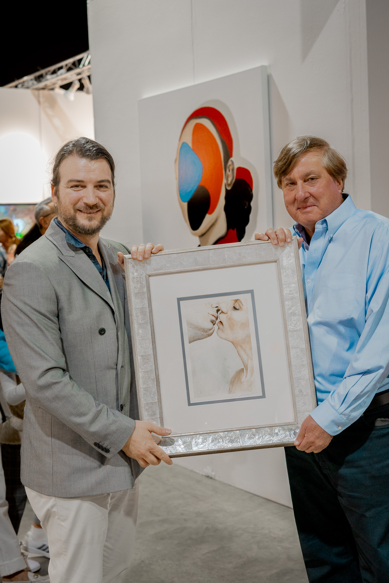 Artist Alex Righetto on the left, presenting the framed painting 'The Kiss' to Nicholas Gravante on the right, at Spectrum Miami 2023.