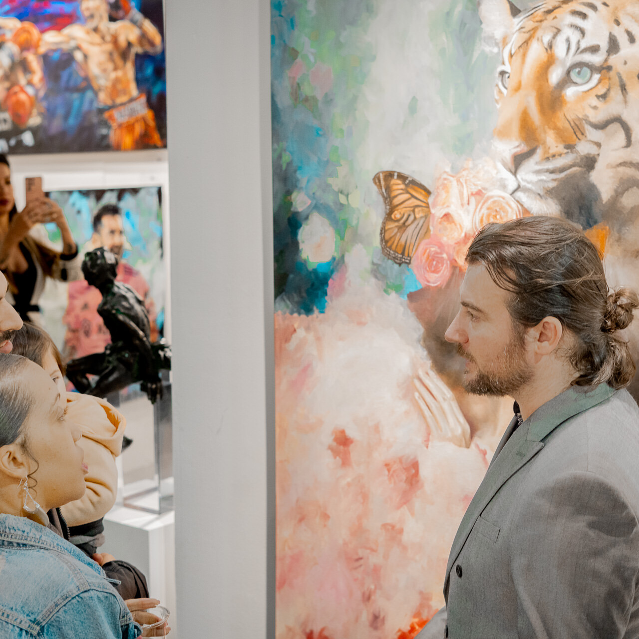 Visitors engage in conversation with artist Alex Righetto at Spectrum Miami, with the striking 'The Guardian' painting in view.