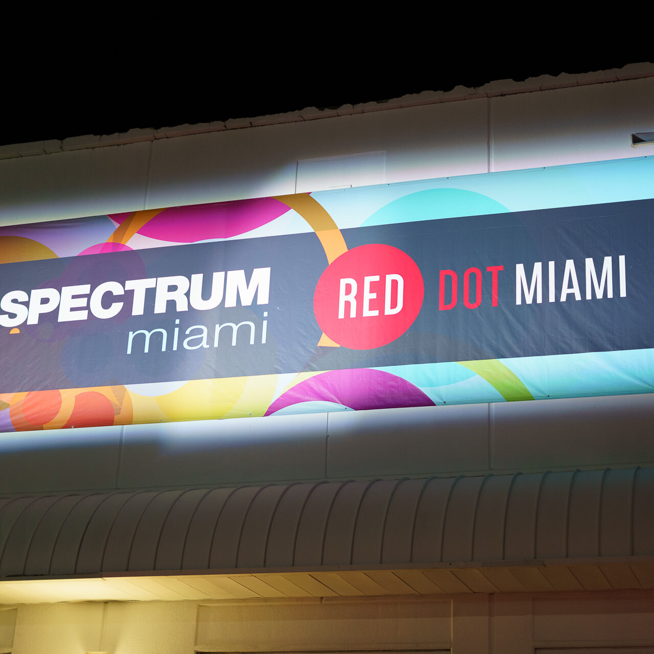 The brightly lit sign for Spectrum Miami and Red Dot Miami art fairs against the evening sky, symbolizing the vibrant art scene of the city.