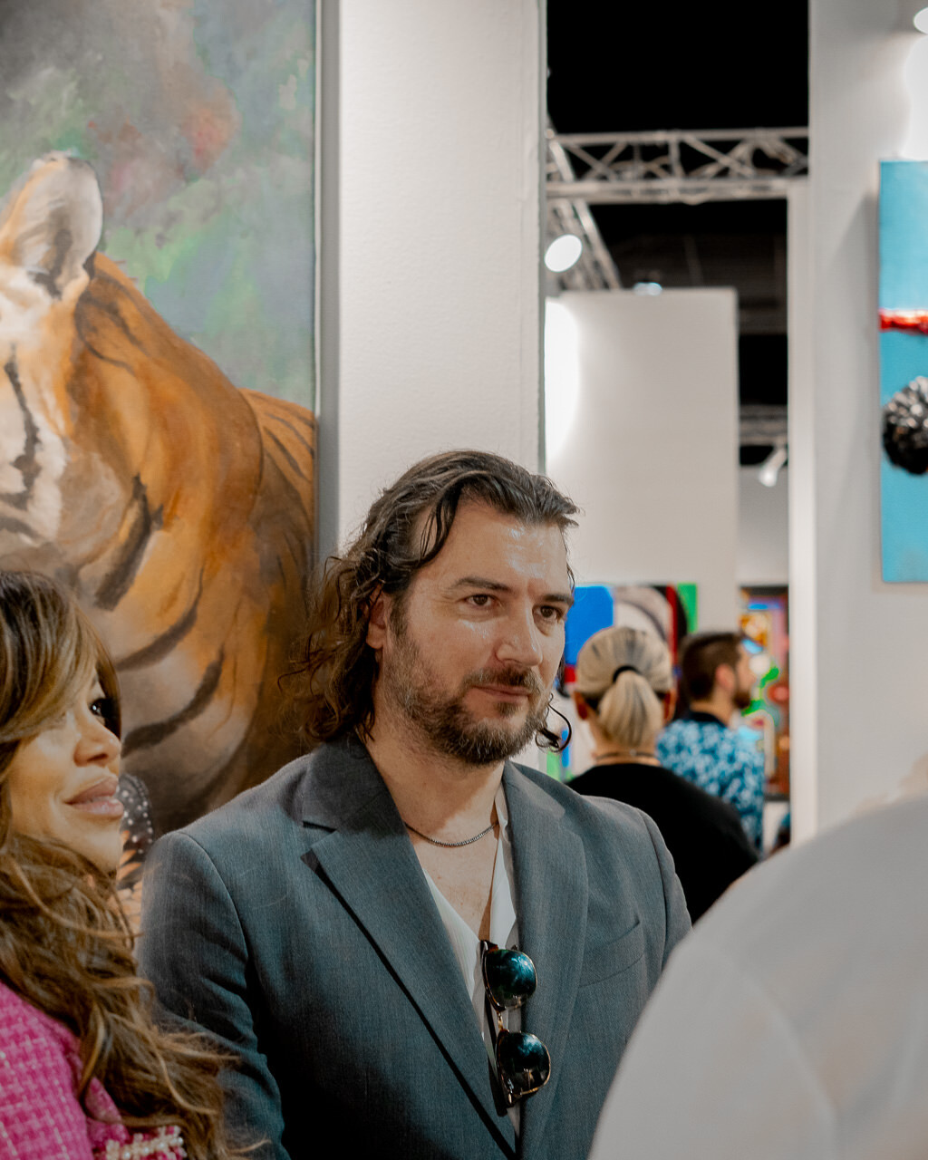 Artist Alex Righetto stands engaged with a group of attendees at Miami Art Week, with his painting 'The Guardian' adding a layer of artistic depth in the background.