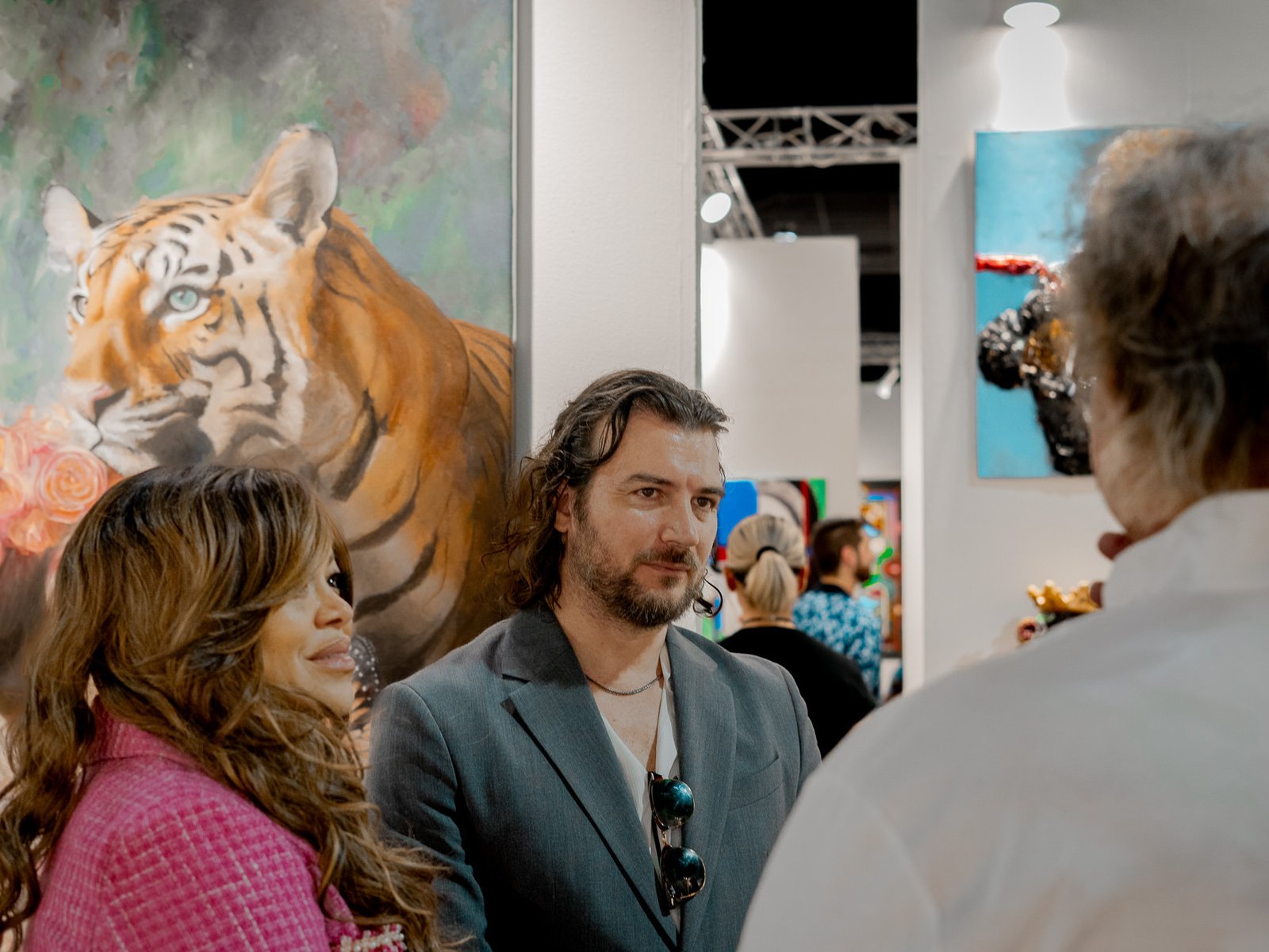 Miami Art Week Recap 3 Artist Alex Righetto stands engaged with a group of attendees at Miami Art Week, with his painting 'The Guardian' adding a layer of artistic depth in the background.
