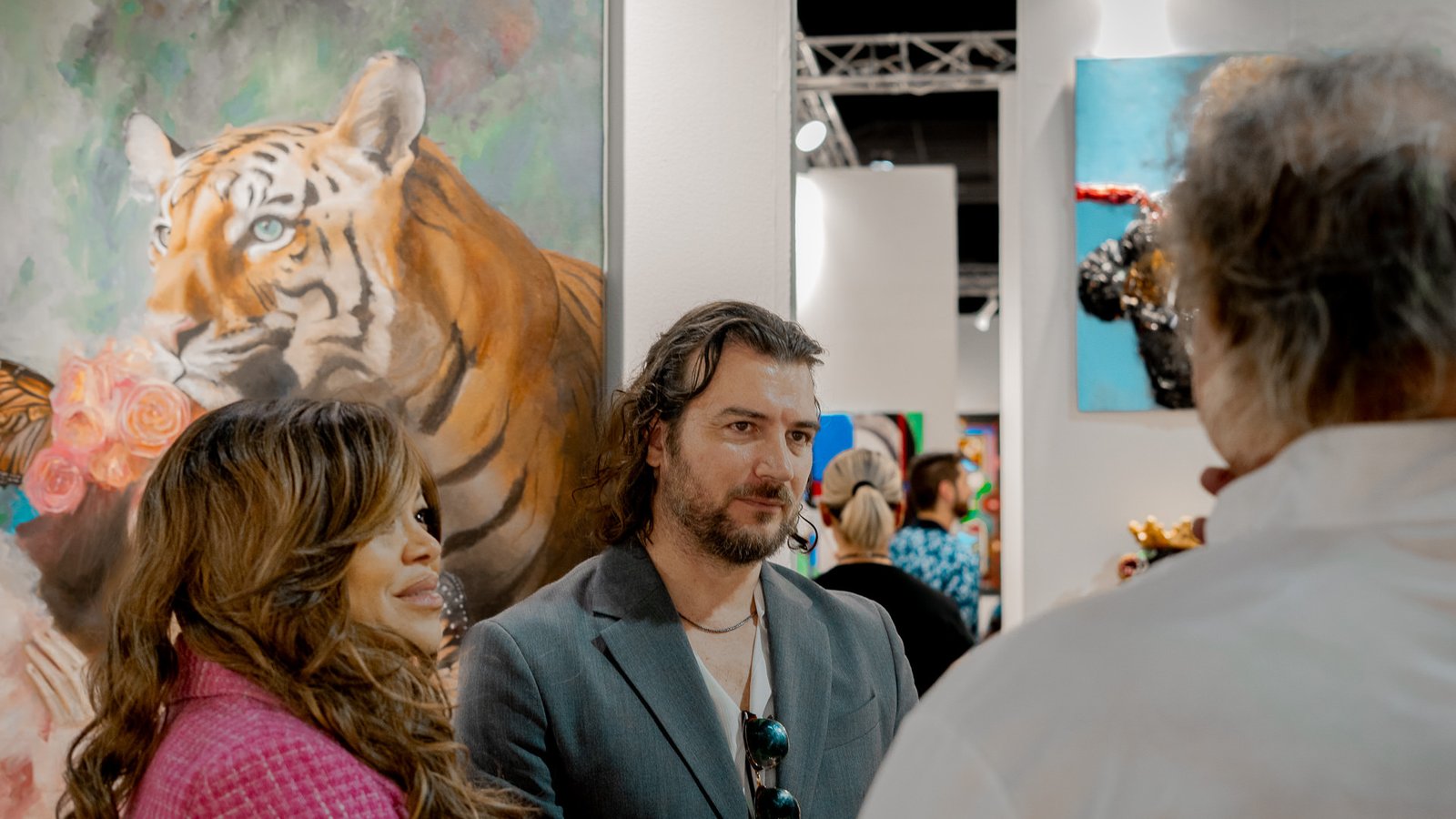 Miami Art Week Recap 4 Artist Alex Righetto stands engaged with a group of attendees at Miami Art Week, with his painting 'The Guardian' adding a layer of artistic depth in the background.