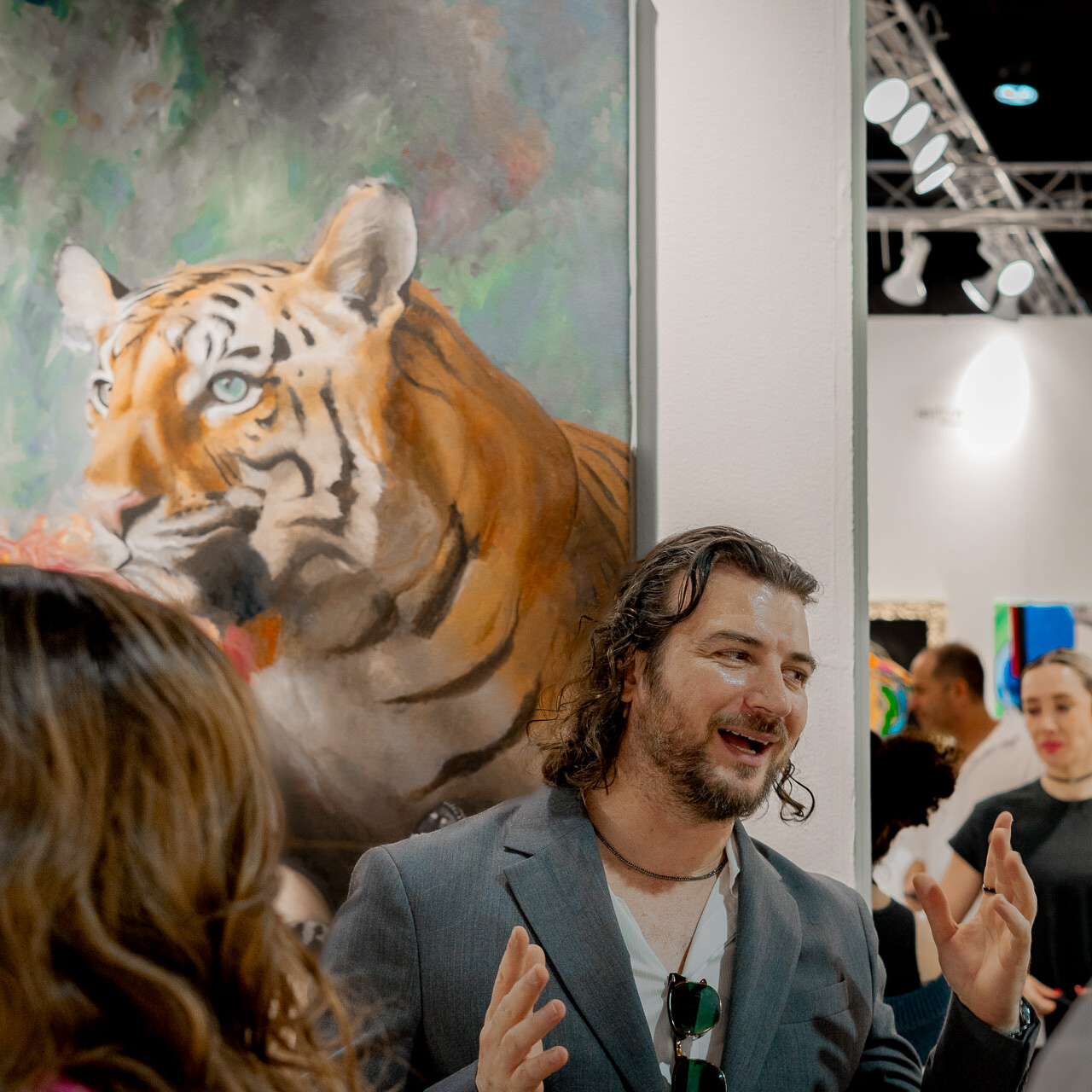 Alex Righetto is seen passionately discussing his artwork 'The Guardian' with art week attendees, with the vivid painting serving as a backdrop.