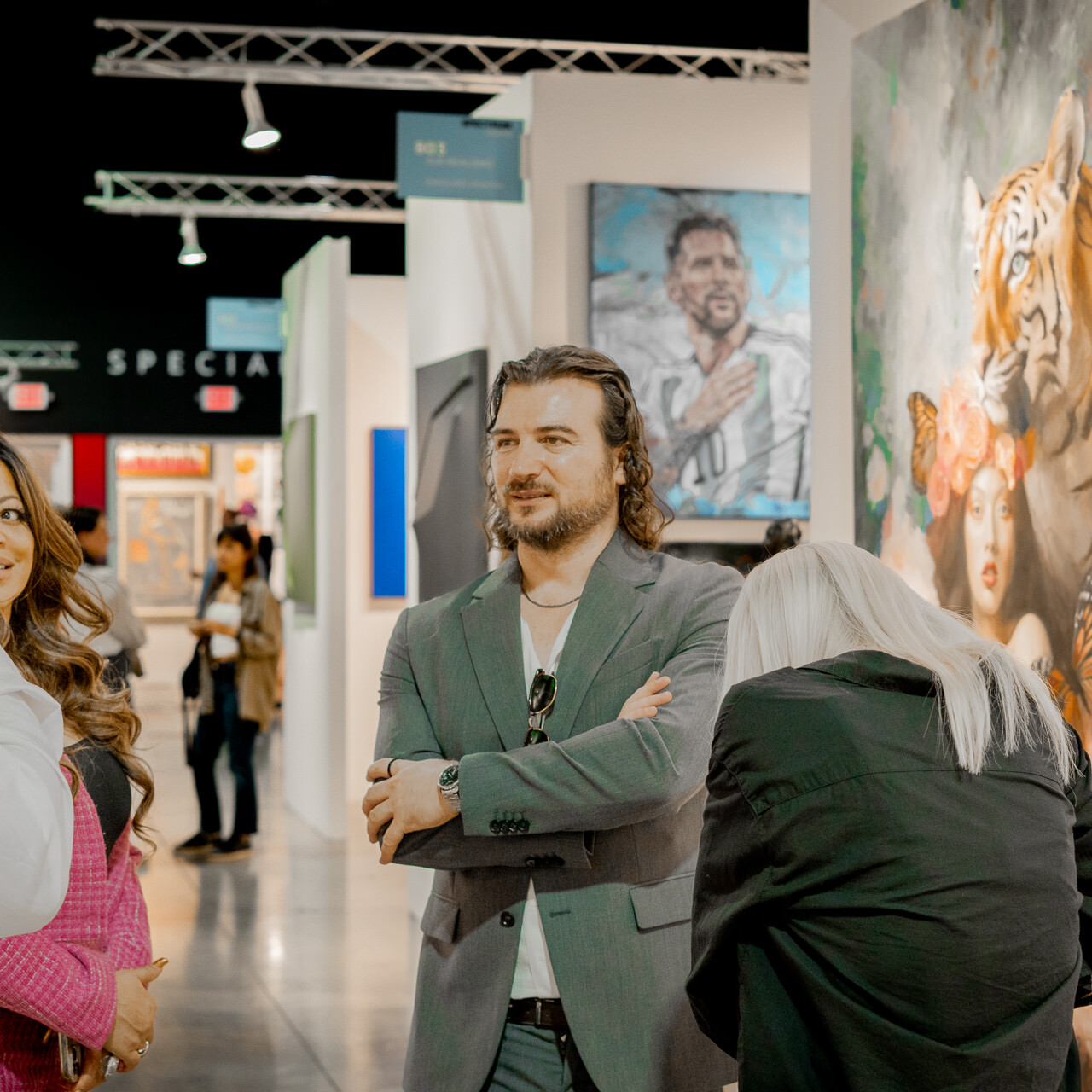 Artist Alex Righetto is engaged in a lively discussion with attendees at Miami Art Week, with the striking painting 'The Guardian' in the background.