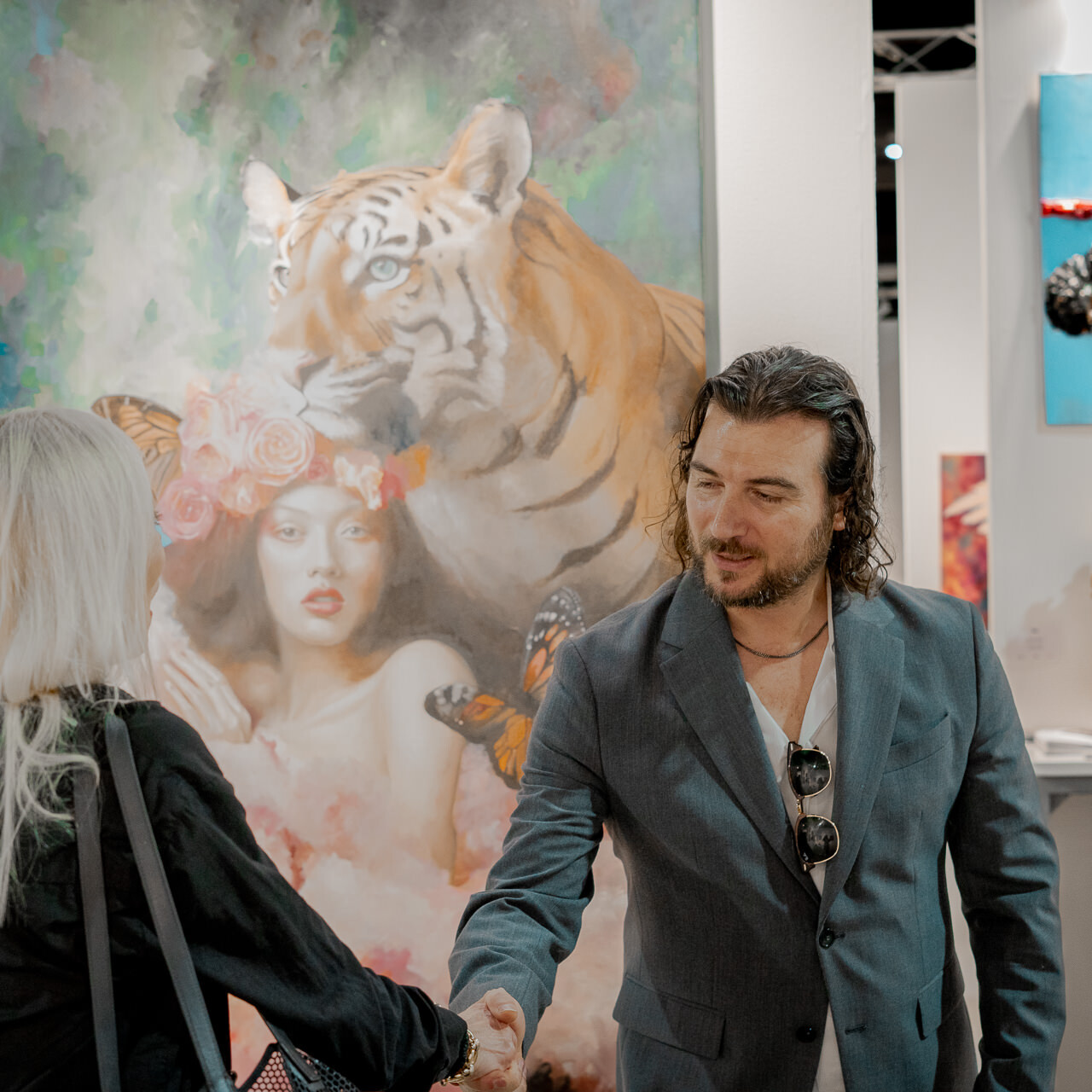 Artist Alex Righetto warmly shakes hands with a visitor against the backdrop of his vibrant painting 'The Guardian' during Miami Art Week.