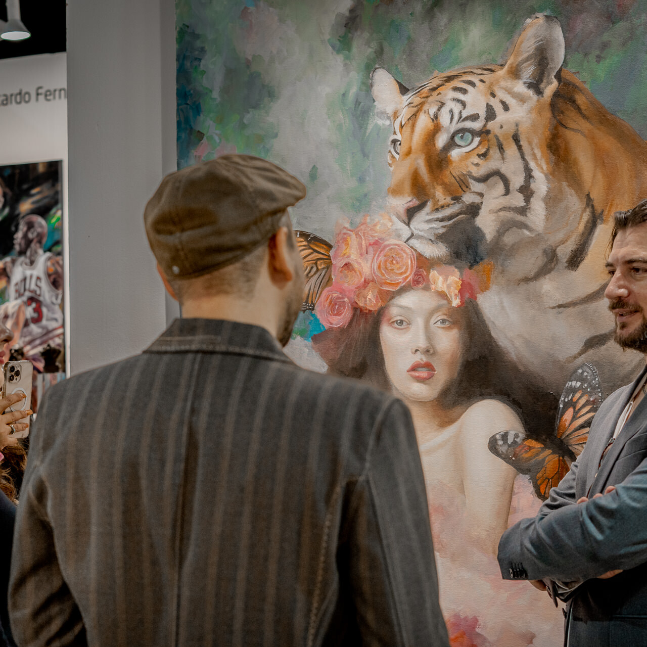 Alex Righetto speaks with two attendees at Miami Art Week, explaining the inspiration behind his painting 'The Guardian'.