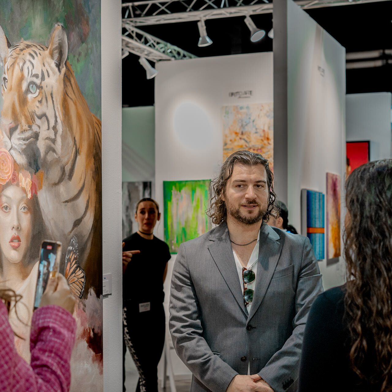 Artist Alex Righetto discusses his work with attendees at Miami Art Week, with 'The Guardian' painting prominently featured.