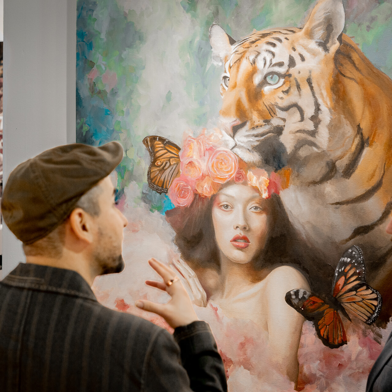 A man listens intently to artist Alex Righetto at an art exhibition with 'The Guardian' in the background, illustrating the power of art to captivate and tell stories.