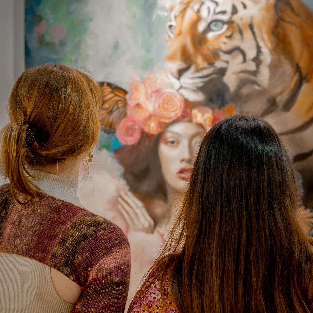 Two attendees are engrossed in observing 'The Guardian,' a painting by Alex Righetto, their backs to the viewer, creating a moment of connection with the artwork.